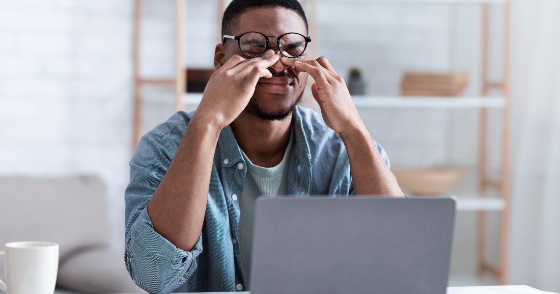 Man Massaging Eyes After Work On Computer At Workplace