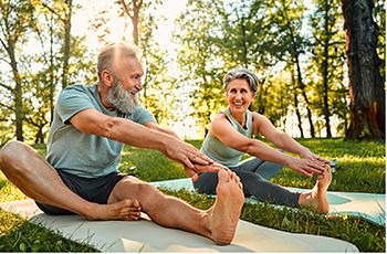 Two older people stretching on the ground outside