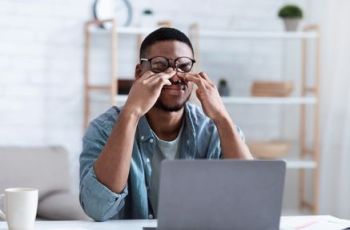 Man Massaging Eyes After Work On Computer At Workplace